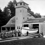 The Coast Guard has been a presence in Charlevoix for over a century. In 1899 the city sold land on the south channel bank near the Lake Michigan Beach to the U. S. Life-Saving Service for one dollar. In 1900 this towered station was commissioned. It opened in 1901. Seven men and a captain manned the building, grounds, and boats for the first several years. In 1962, the Coast Guard moved into a new building on the north bank of the upper channel next to the railroad bridge. The shingled station was taken down in 1965, the ground leveled, and the property reverted to the city U.S. Life Saving Station