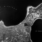 Charlevoix from approximately 25,000 feet. The town straddles an isthmus less than a mile wide, divided by a man-made waterway called Pine River. This consists of the lower channel that leads to Lake Michigan (left) and the upper channel to Lake Charlevoix (right), the two connected by what is known as Round Lake. The settlement was originally called, like its waterway, Pine River, named so by the itinerant fisherman who first settled here for part of each year. A major landmark for them was thought to be a tall pine tree on the bluff overlooking Lake Michigan. Charlevoix Map