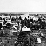 In winter, logs were brought to the mill from the lumber camps of southern Charlevoix County by horse-drawn sledges. They entered town on State Street, seen here between Mason and Clinton Streets, turned right onto Main Street (later Park Avenue), traveled one block to Bridge Street, turned left, crossed the bridge, went up the north hill, turned right onto East Dixon Avenue and reached the lumber company’s property. If necessary, streets were watered down to freeze for the gliding transport of these gigantic loads. Charlevoix County Horse-Dawn Sledges