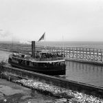 The Thomas Friant, which ran between Harbor Springs, Petoskey, Charlevoix, and East Jordan, was one of the busiest boats of the area. Barely visible above her bow awning, just under the topmost trestle railing, appear the remains of the once great Fox & Rose dock, now much broken apart and disintegrating. The Thomas Friant